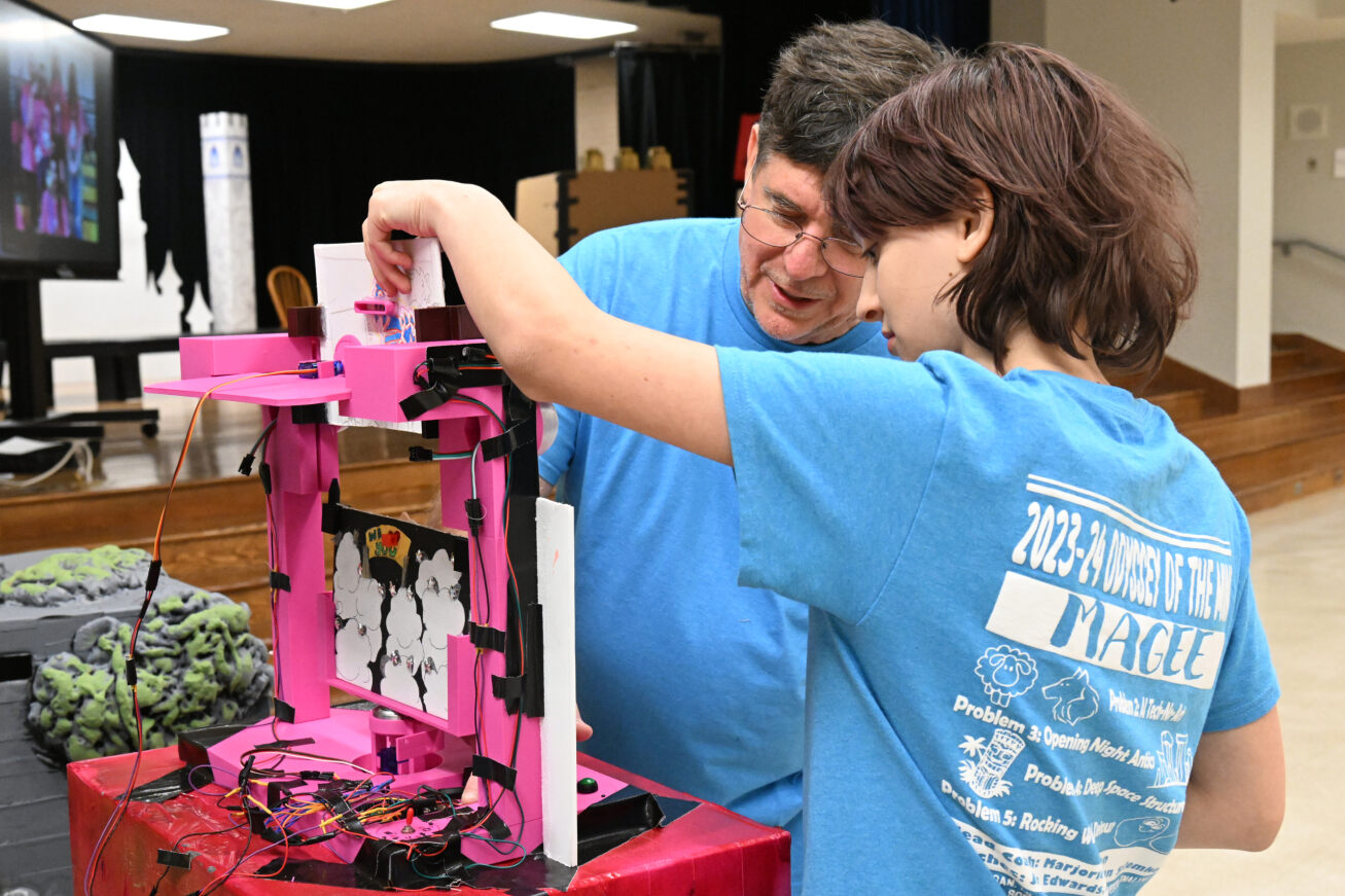 A student and teacher in blue shirts look at a bright pink contraption