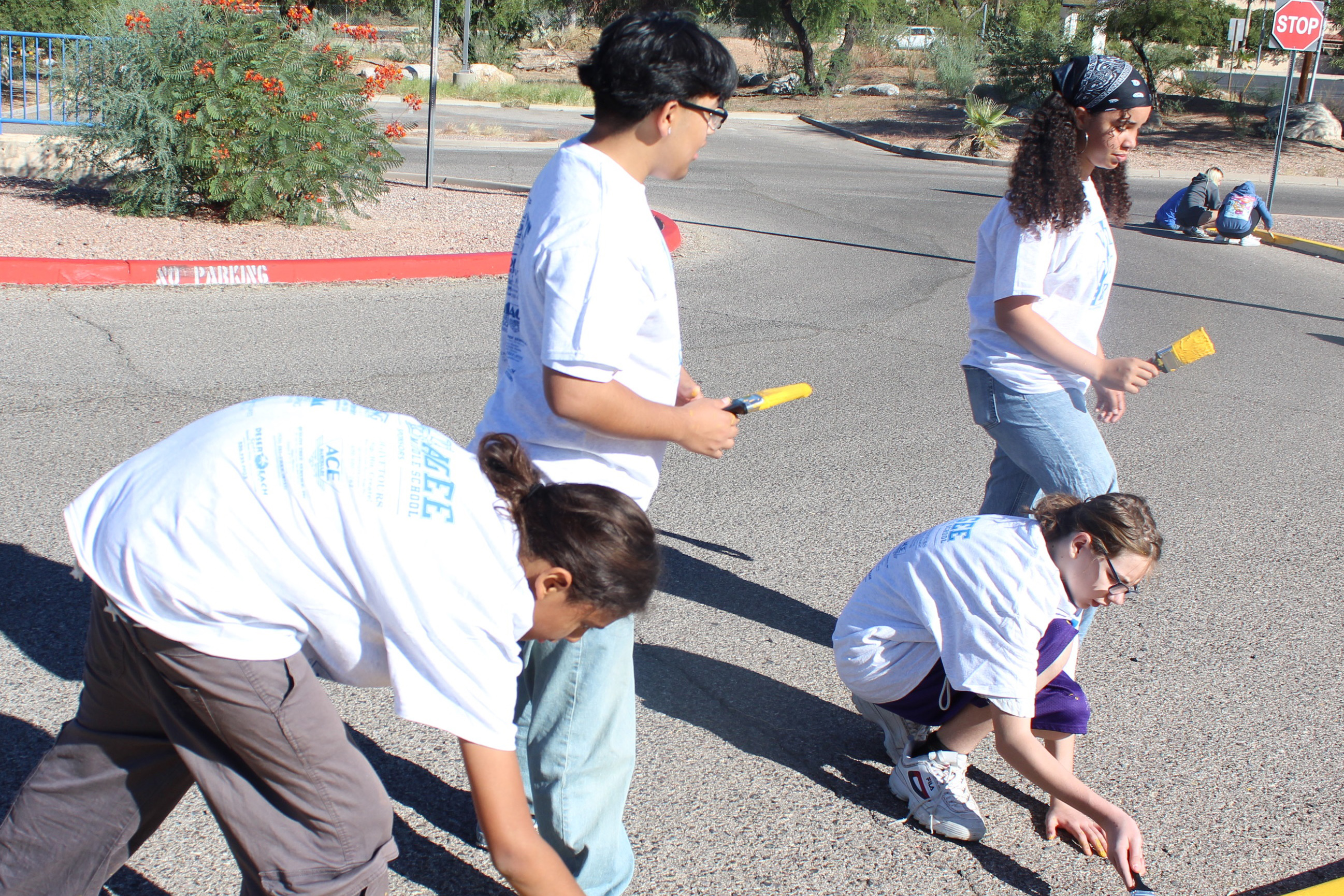 Four students repaint the curb with yellow paint