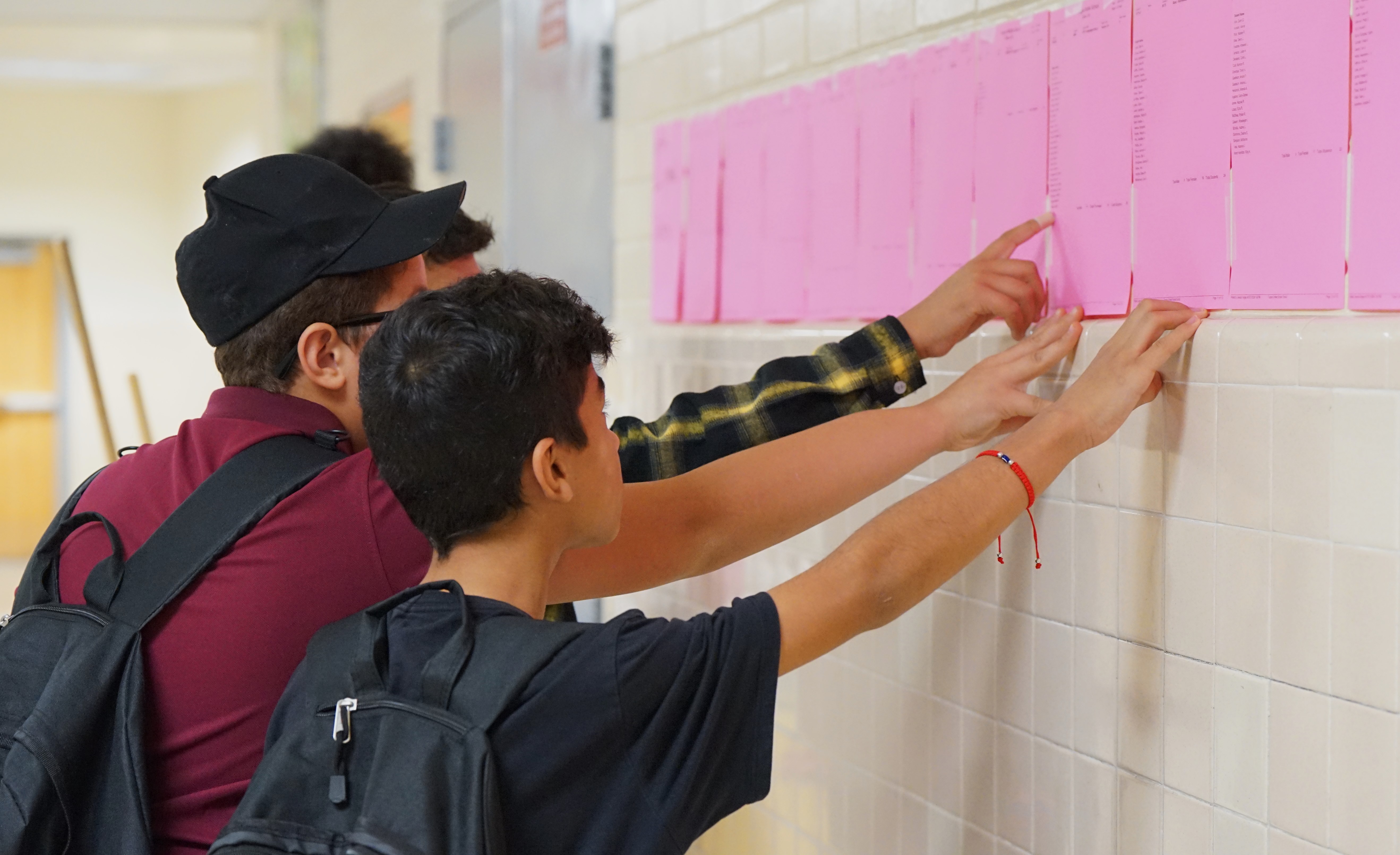 Two boys point at their schedule on a wall in the hallway